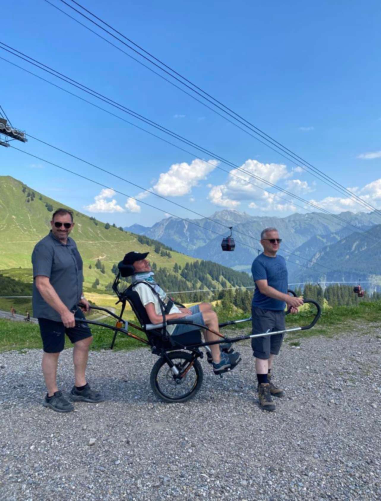 Zwei Männer mit einem Wanderrollstuhl in einer malerischen Berglandschaft